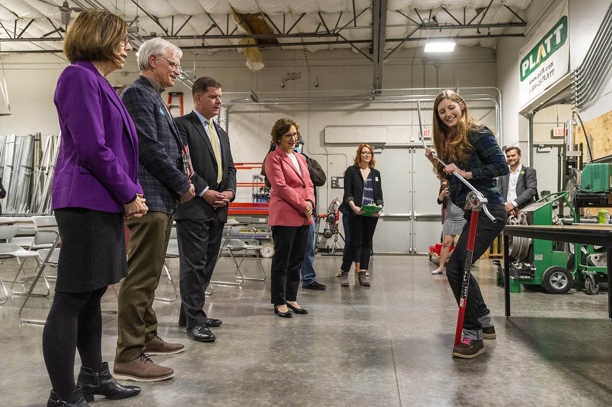 An apprentice demonstrates a hand conduit bender in an electrical training shop during a US Department of Labor visit