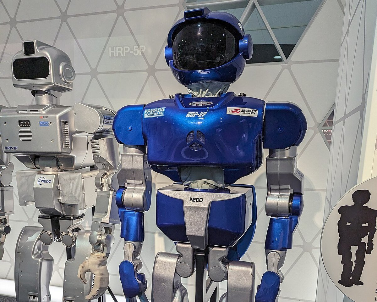 Two humanoid research robots, HRP-2P in blue and HRP-3P in silver, standing on display stands at Science Square Tsukuba in Japan