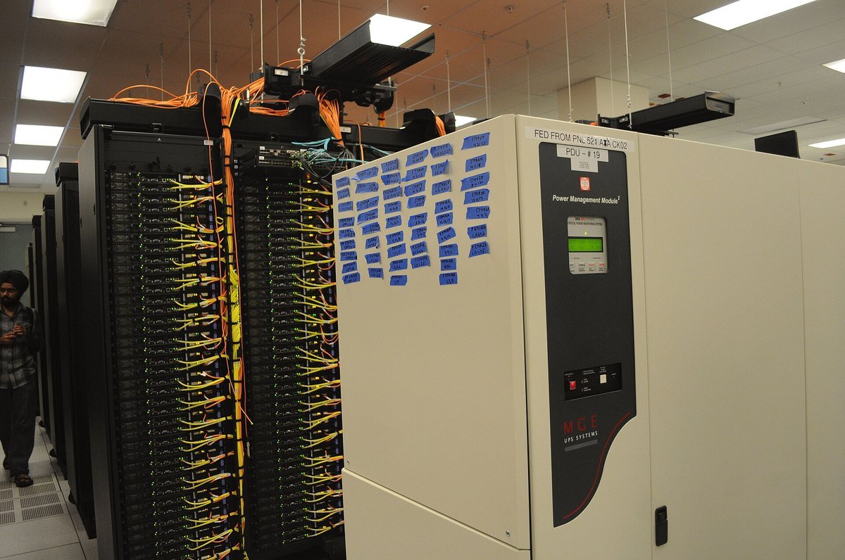Power distribution unit and racks of network cabling in a data center, with hand-written circuit labels on blue tape