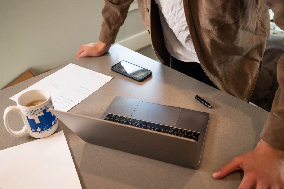 A closed laptop, papers and a coffee mug on a kitchen counter