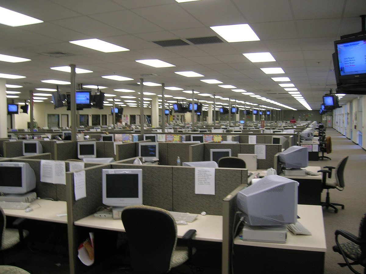 A large empty call-centre floor with rows of cubicles and monitors