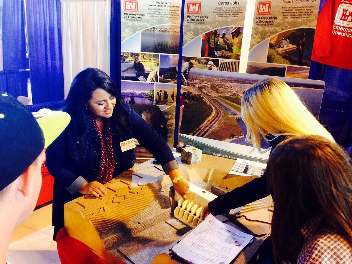 A recruiter leans over a table display talking with two visitors at a careers fair booth