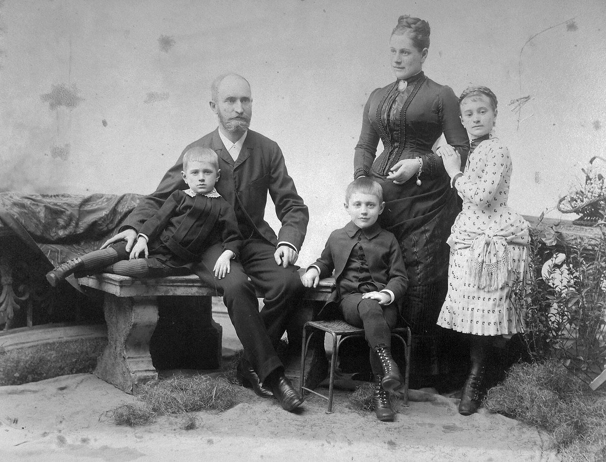 A studio family portrait from around 1900 with visible scratches, stains and a torn emulsion
