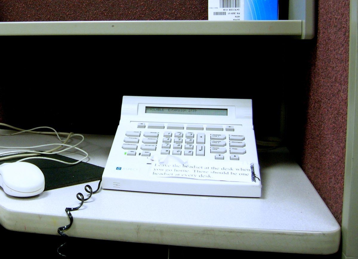 An empty call centre cubicle in Lakeland, Florida. The phone display reads AVAILABLE, extension 2739, and a taped note says to leave the headset at the desk.
