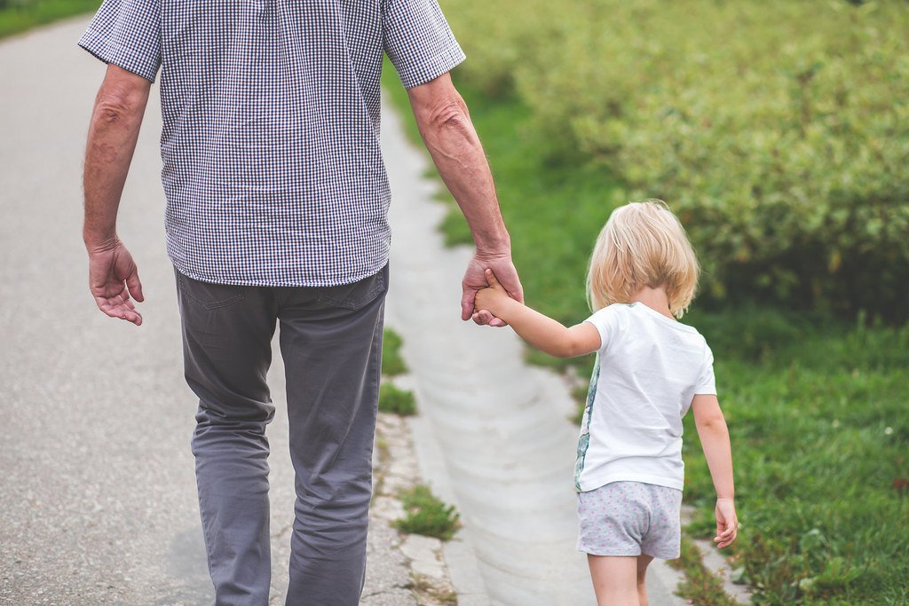 A grandparent and a small child walking away down a path, holding hands, faces not visible