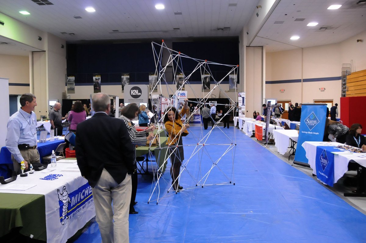 A wide view of a job fair in a hall, with employer booths and recruiters along both sides.