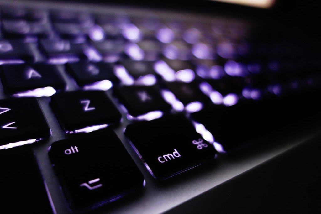 A backlit laptop keyboard glowing in a dark room