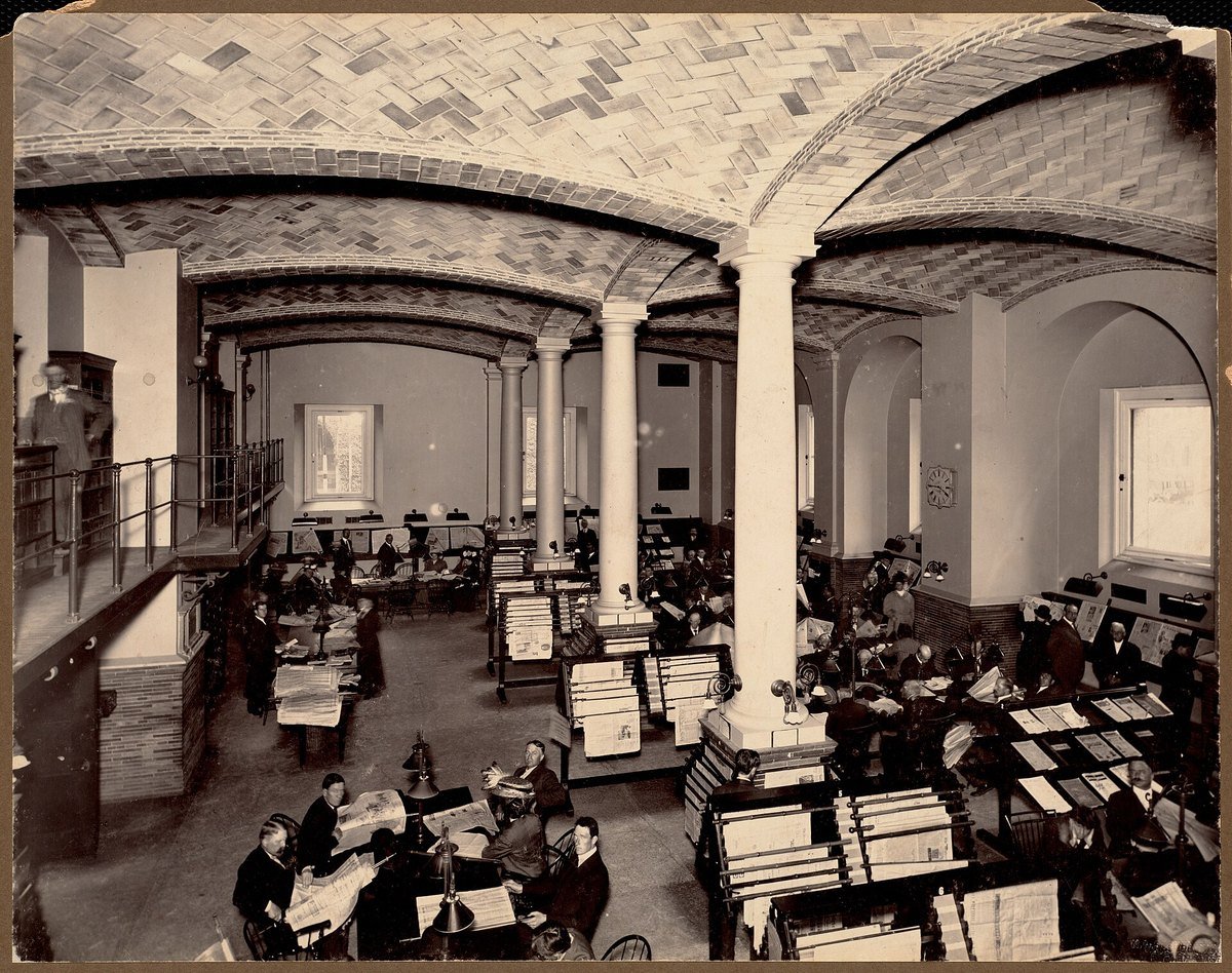 A crowded newspaper reading room at the Boston Public Library around 1900, men and women reading papers at racks