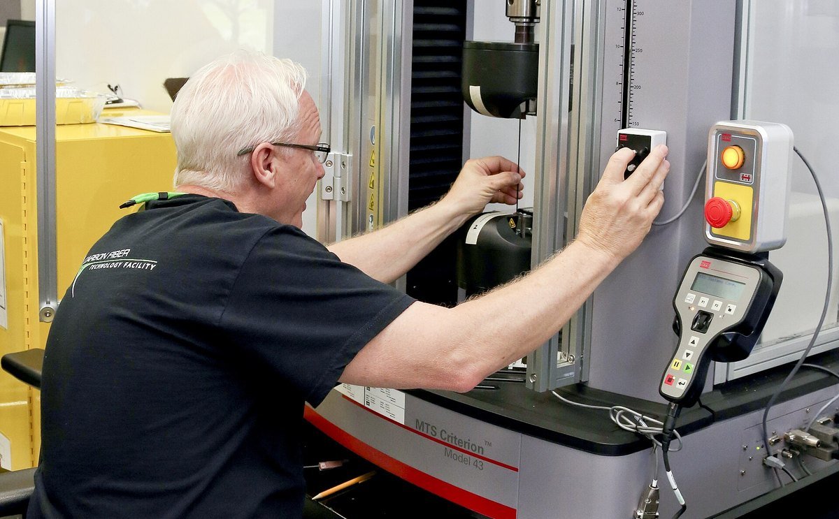 A technician at Oak Ridge National Laboratory operating a tensile testing machine on a carbon fiber sample