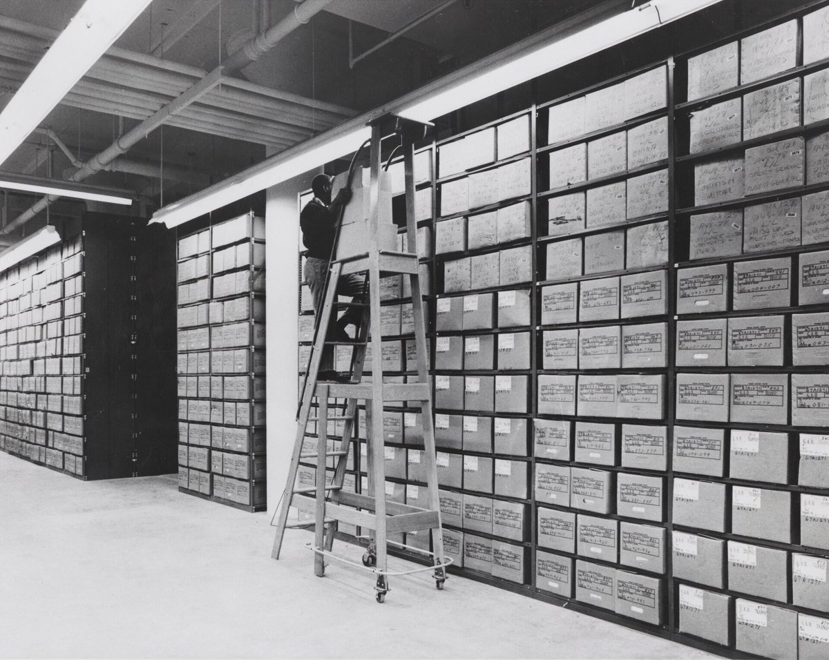 An employee on a rolling ladder retrieving boxes in a federal records centre stack area