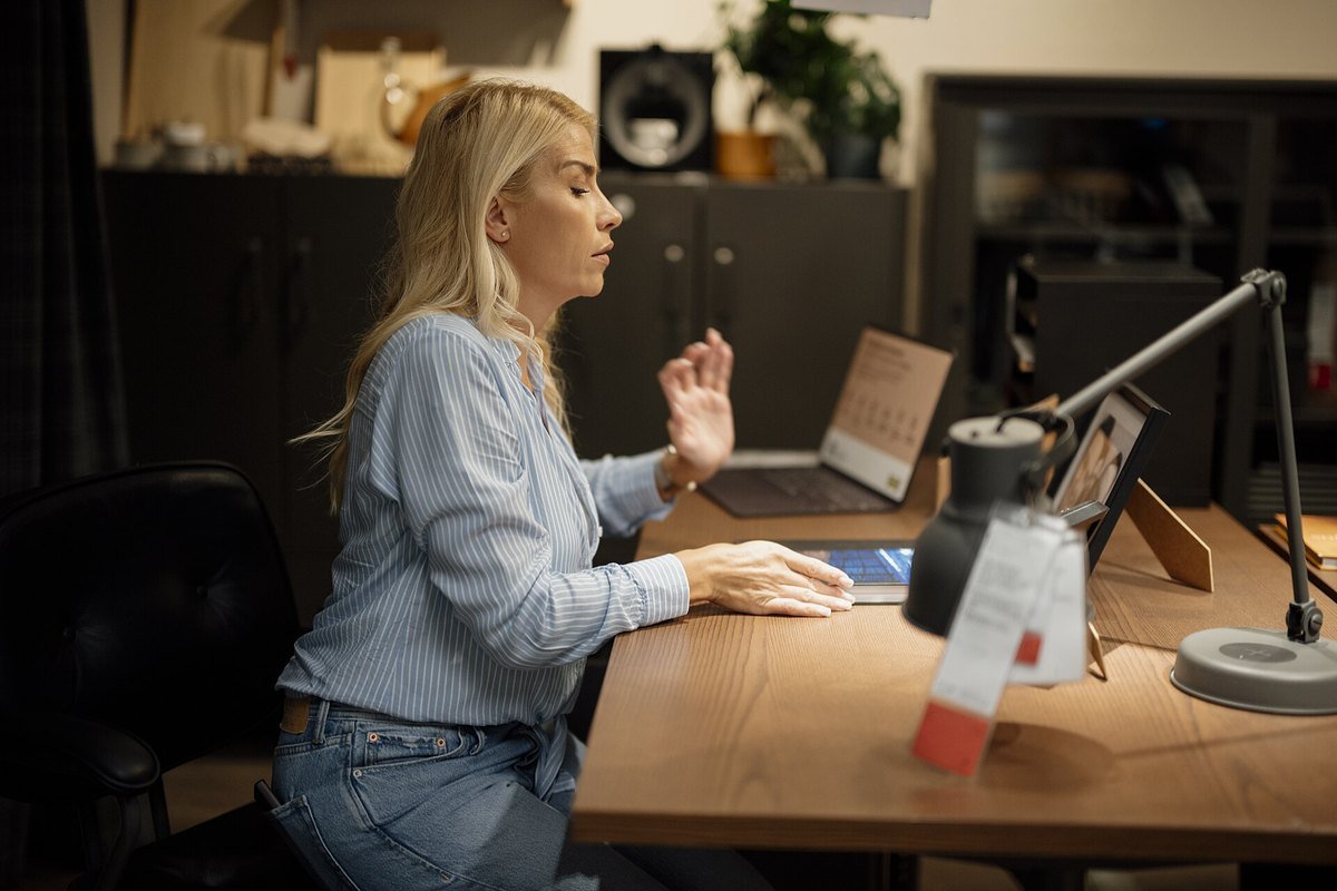 A woman working at a laptop at a wooden desk in a home office
