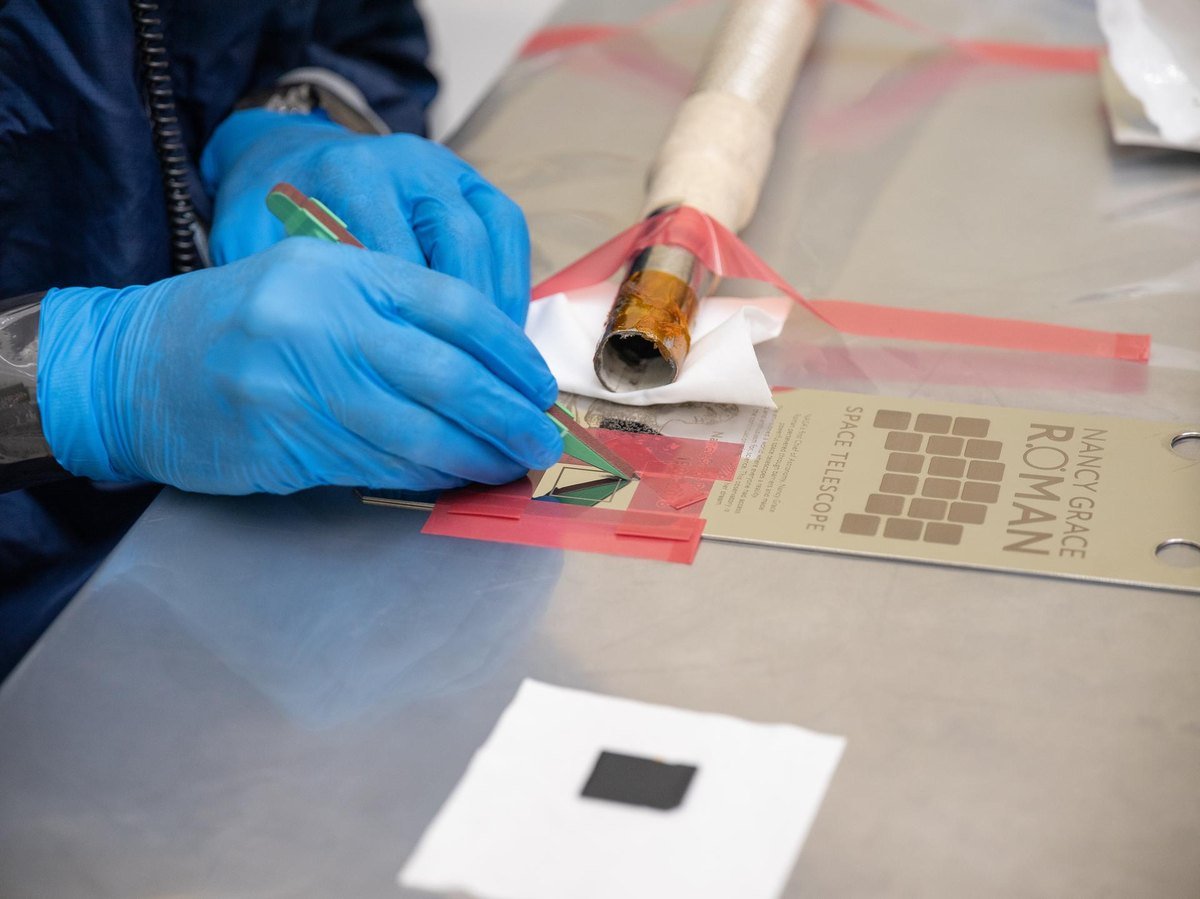 A technician in blue gloves bonding a memory card holding 1,350,144 submitted names onto a commemorative plaque on the Roman Space Telescope
