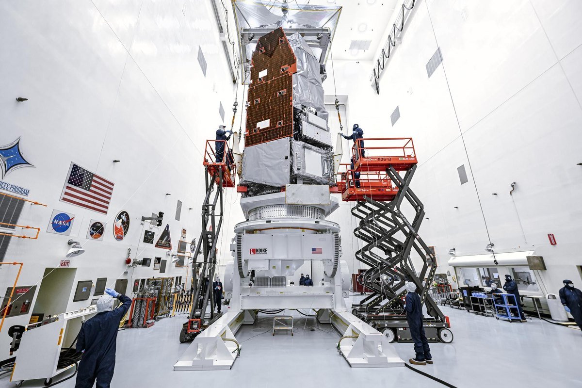 The Nancy Grace Roman Space Telescope standing vertical inside the Payload Hazardous Servicing Facility at NASA Kennedy Space Center, technicians on lifts working beside it
