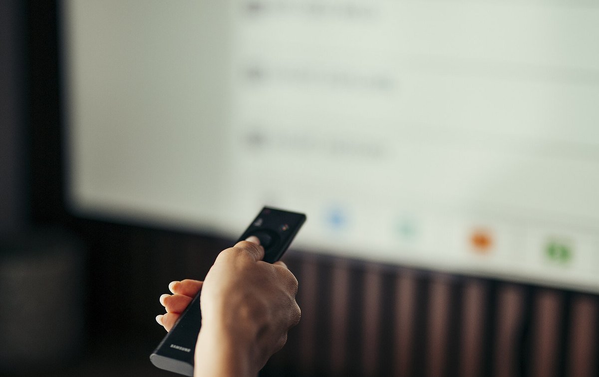 A hand pointing a Samsung remote at a television showing an on-screen settings list