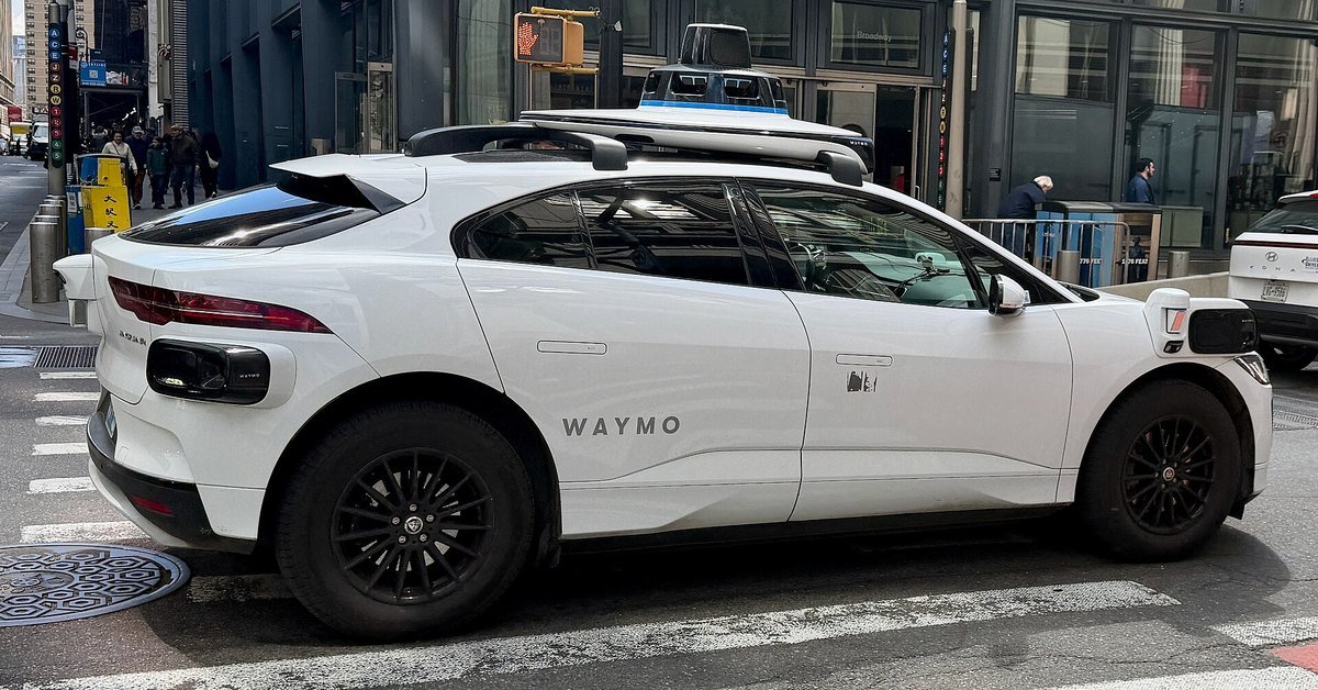 A Waymo Jaguar I-Pace autonomous vehicle with roof sensor array parked on a city street