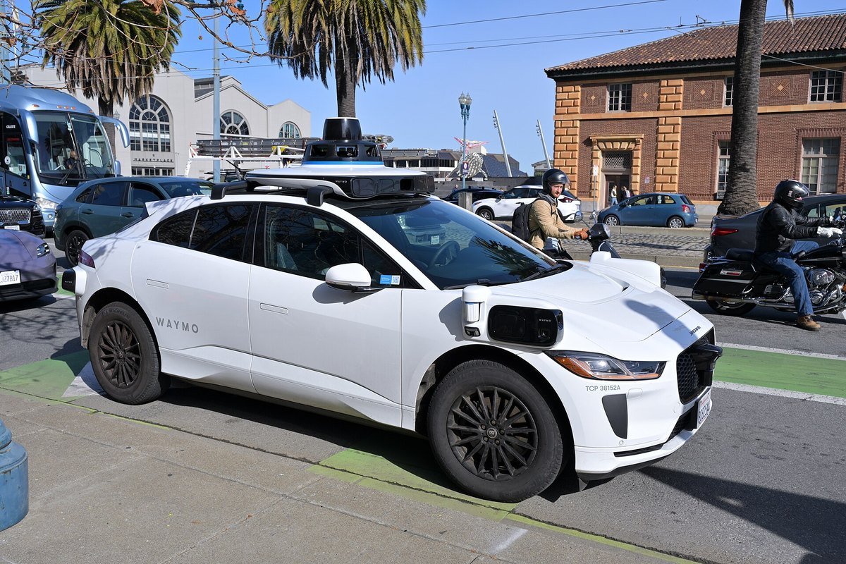 A white Waymo Jaguar I-Pace robotaxi with roof sensors on the Embarcadero in San Francisco, January 2026