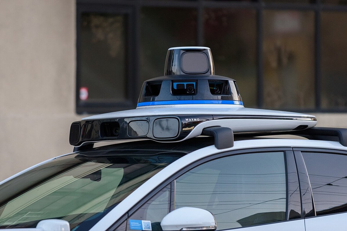 Close-up of the roof sensor pod on a Waymo Jaguar I-Pace, showing the spinning lidar unit, camera windows and side sensor housings