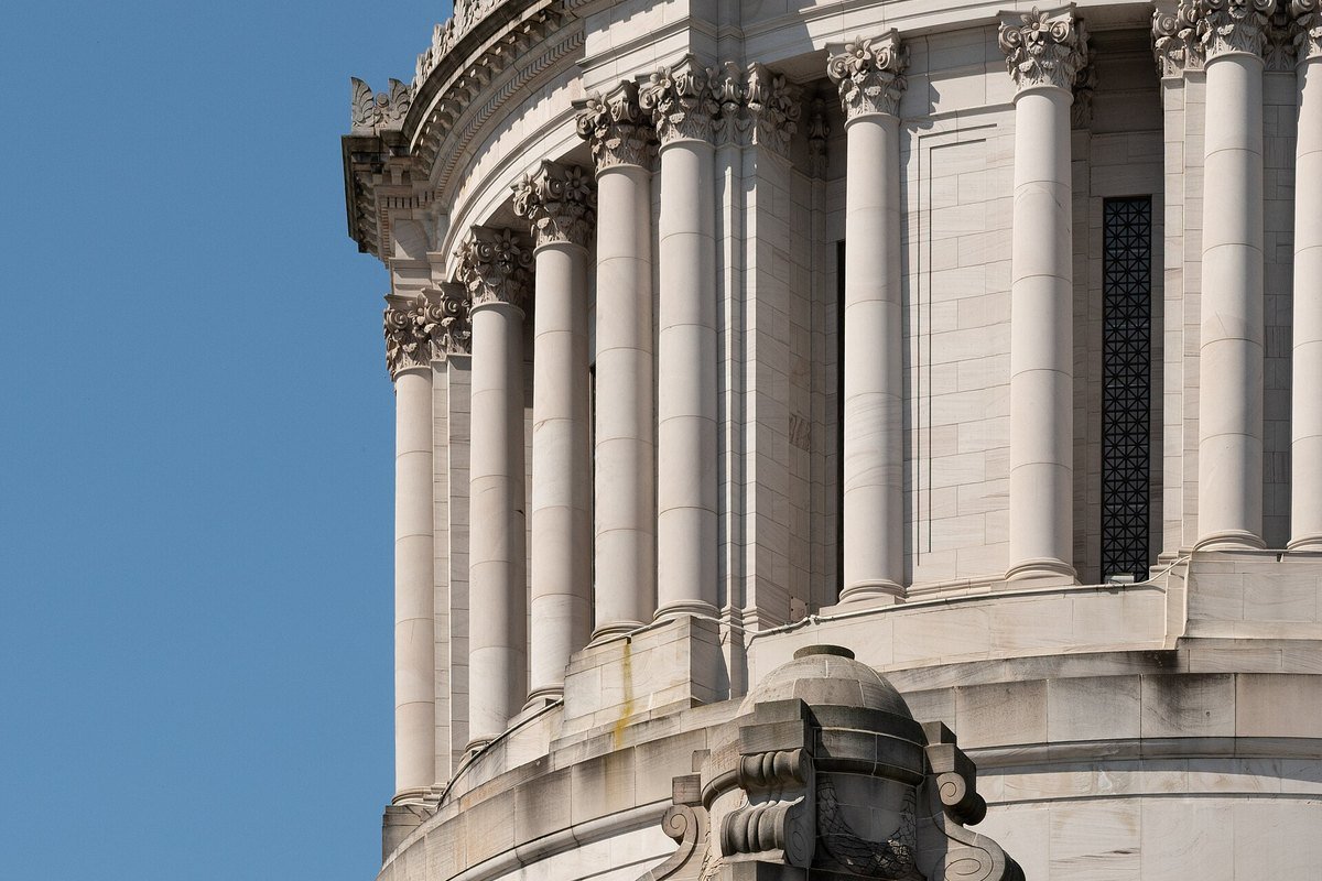 The marble dome and colonnade of the Washington State Capitol in Olympia against a clear blue sky.