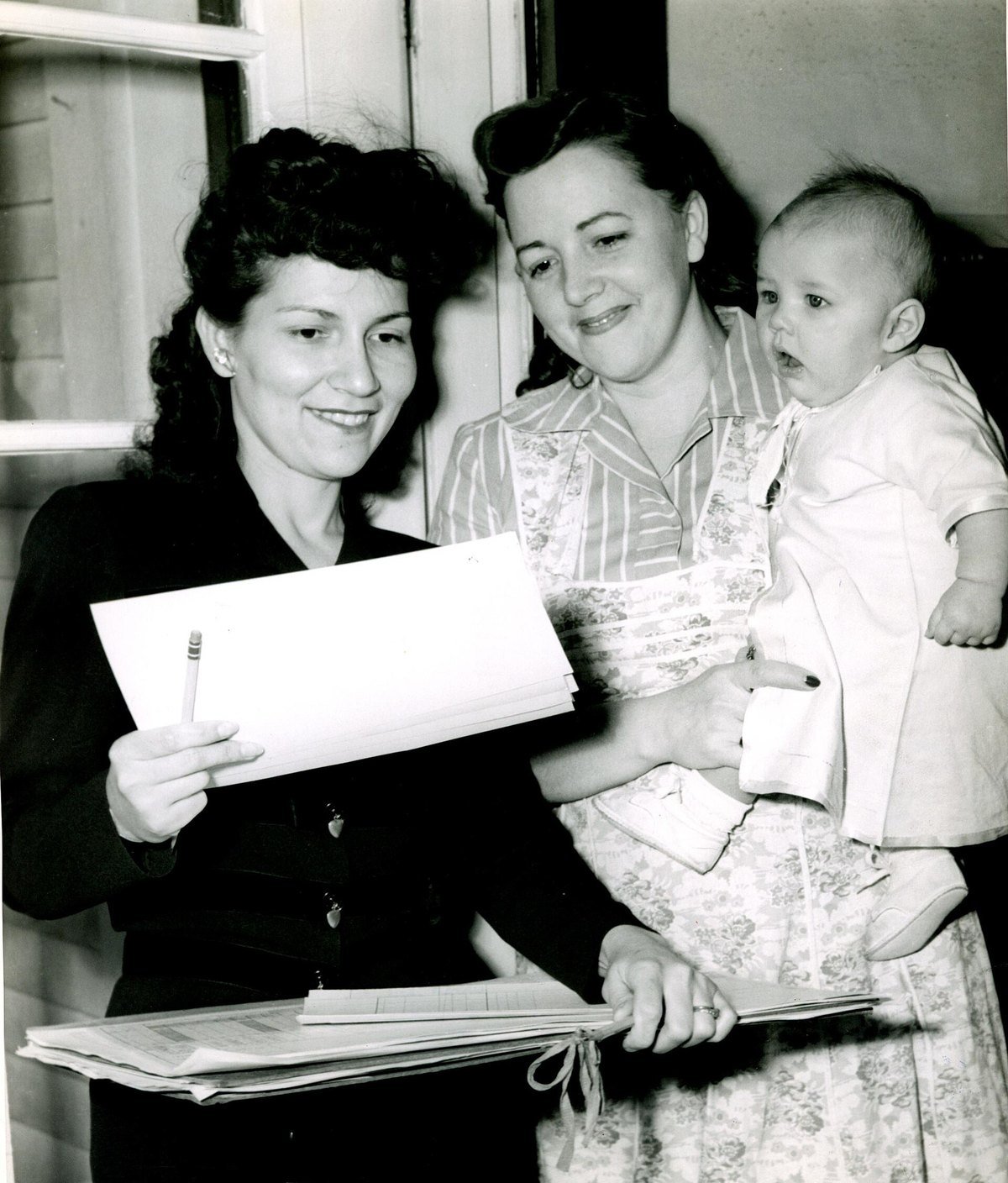 A 1950 census enumerator holding her schedule at a doorway, interviewing a mother holding a baby