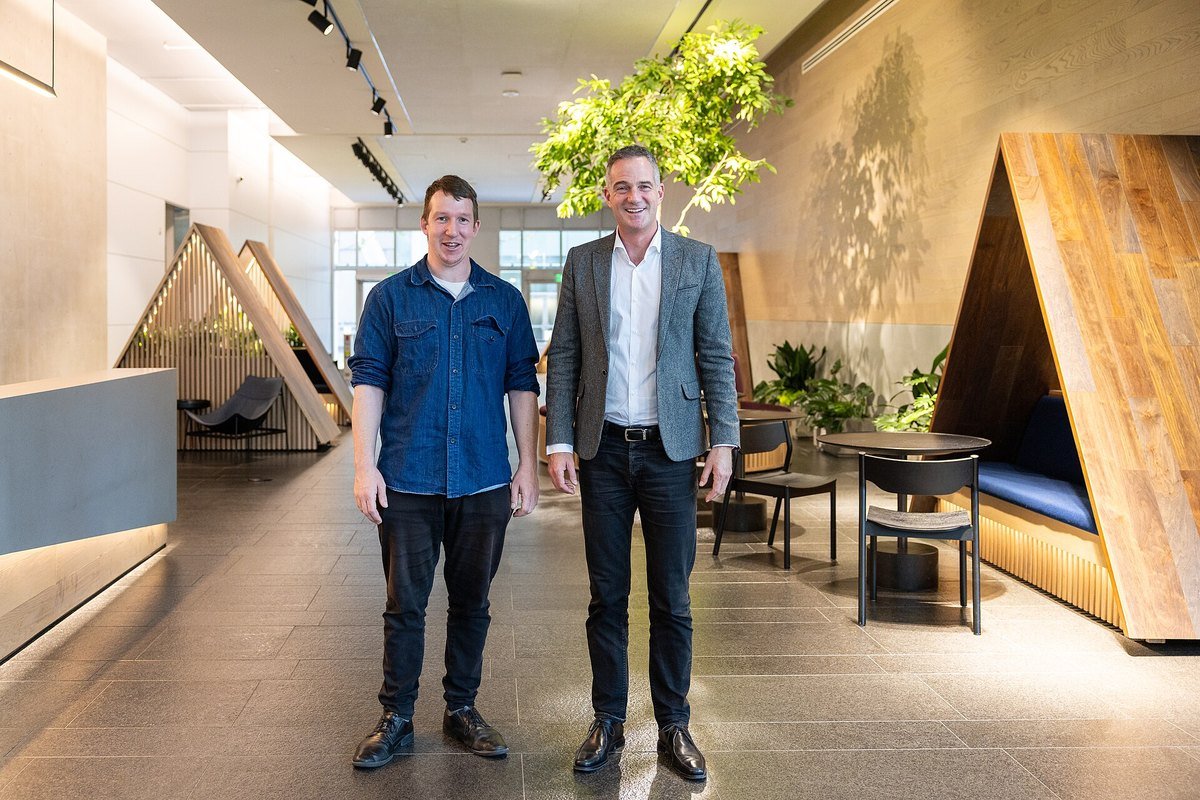 Two men standing in the lobby of Anthropic's office in San Francisco, with wooden booths and plants behind them.