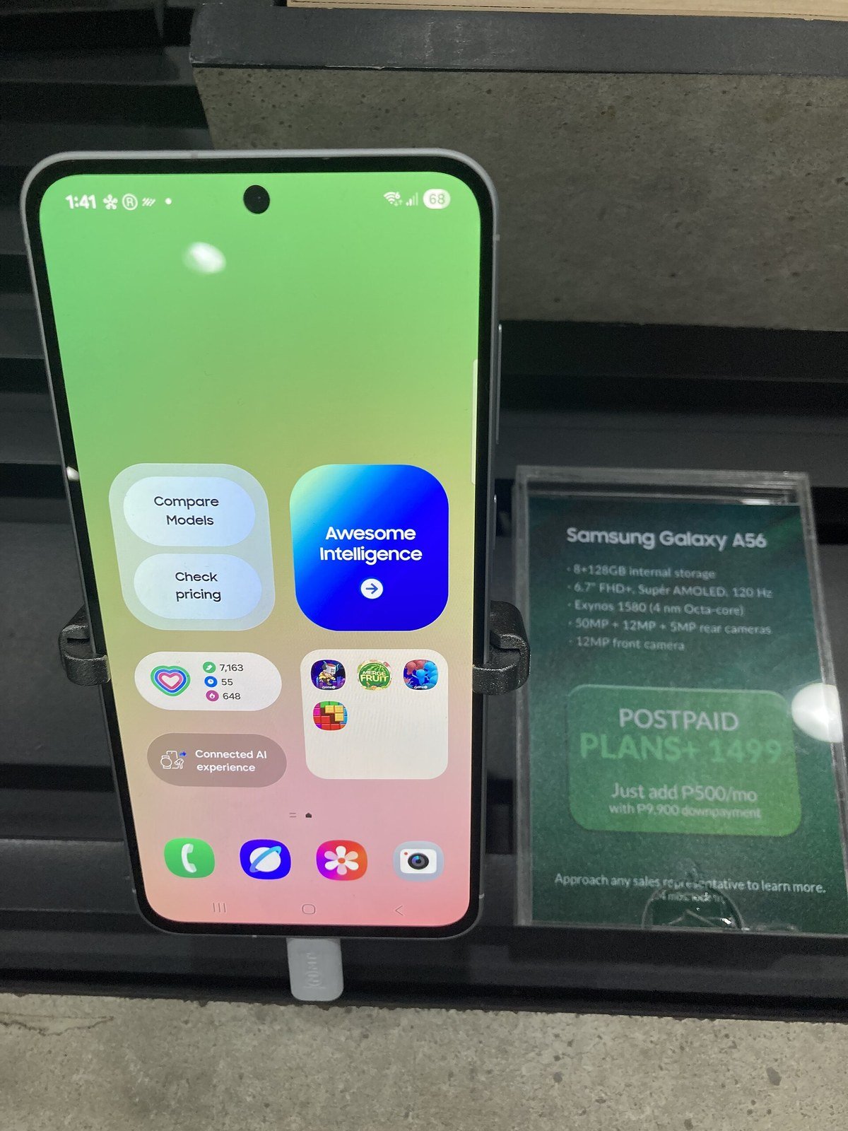 A Samsung Galaxy A56 demo phone in a store, its home screen showing a blue tile labeled Awesome Intelligence.