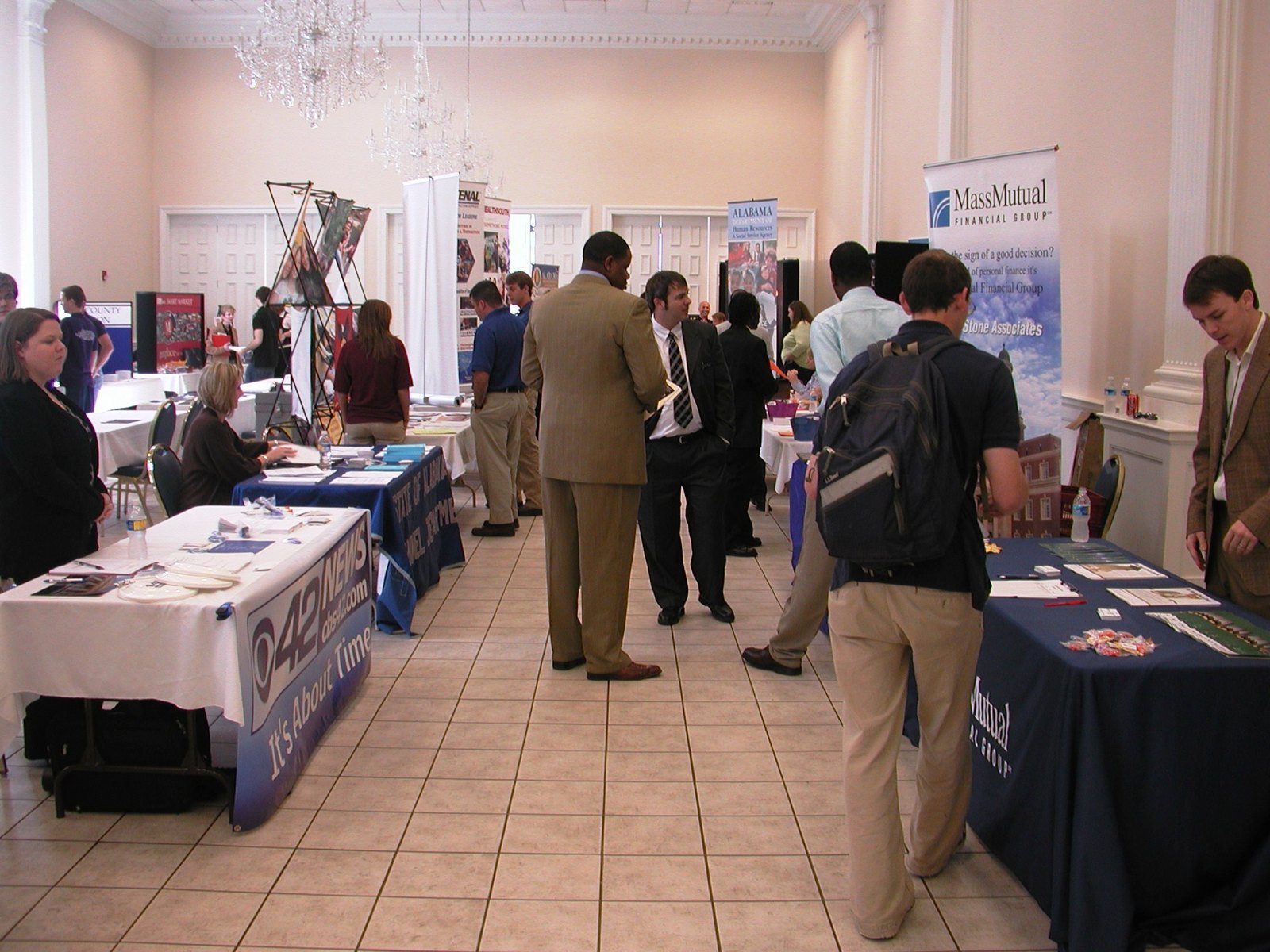 Job seekers walking between recruiter tables at a career fair in a large hall.