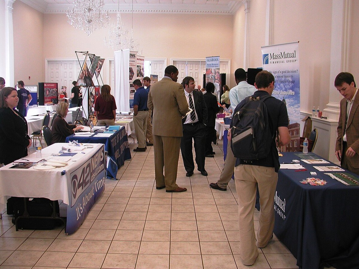 Job seekers walking between employer tables and banners at an indoor career fair