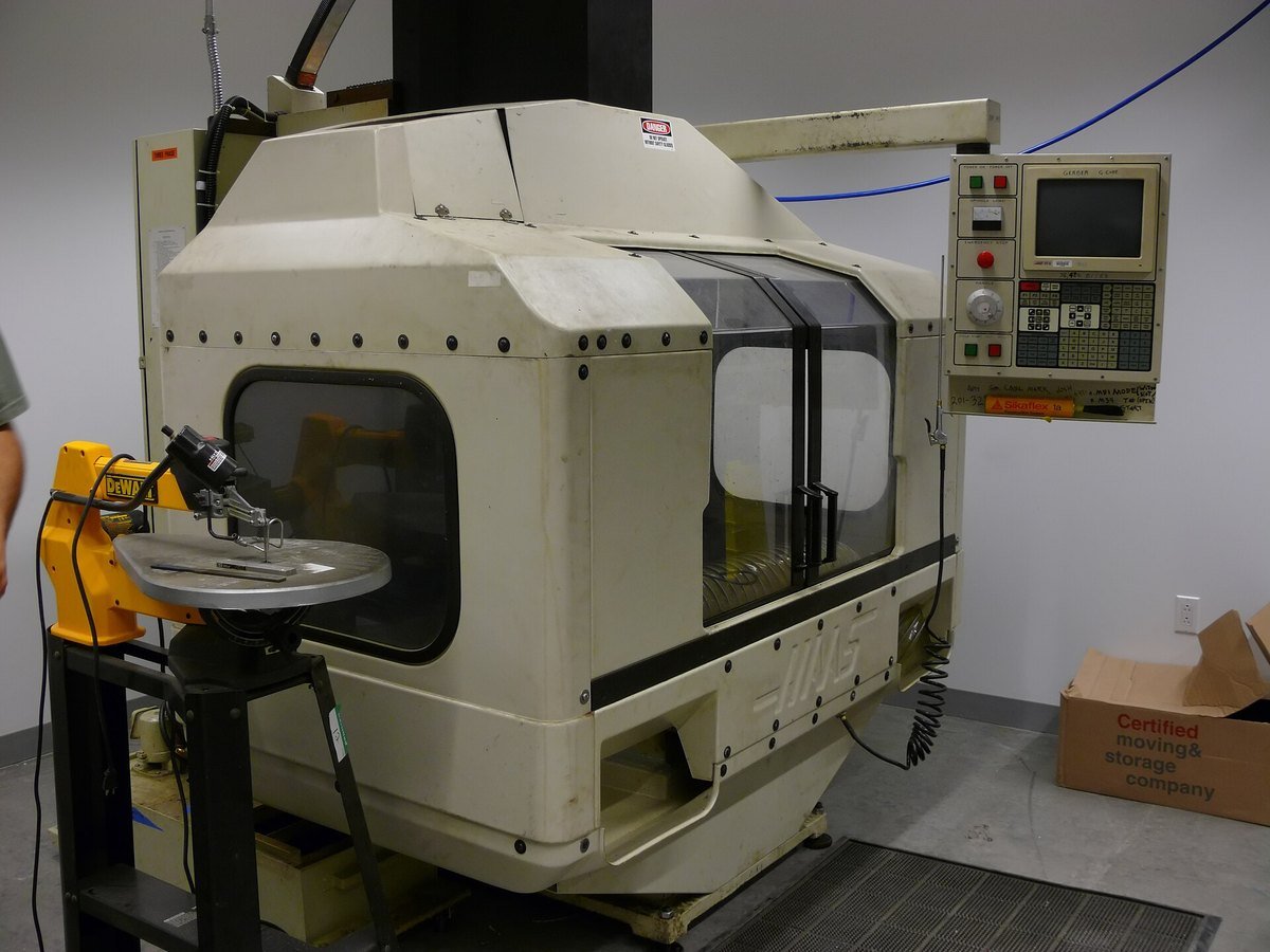 A compact CNC milling machine with a control panel and an enclosed cutting area in a workshop.