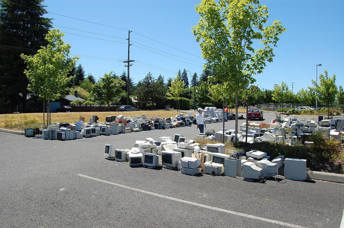 Rows of discarded desktop computers and monitors laid out in a parking lot at a community recycling event.