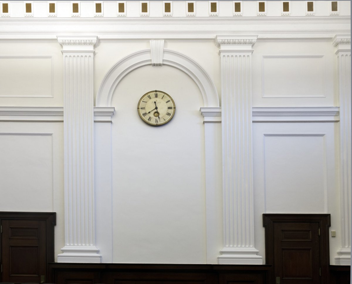 A single antique clock on the white panelled wall of a federal courtroom