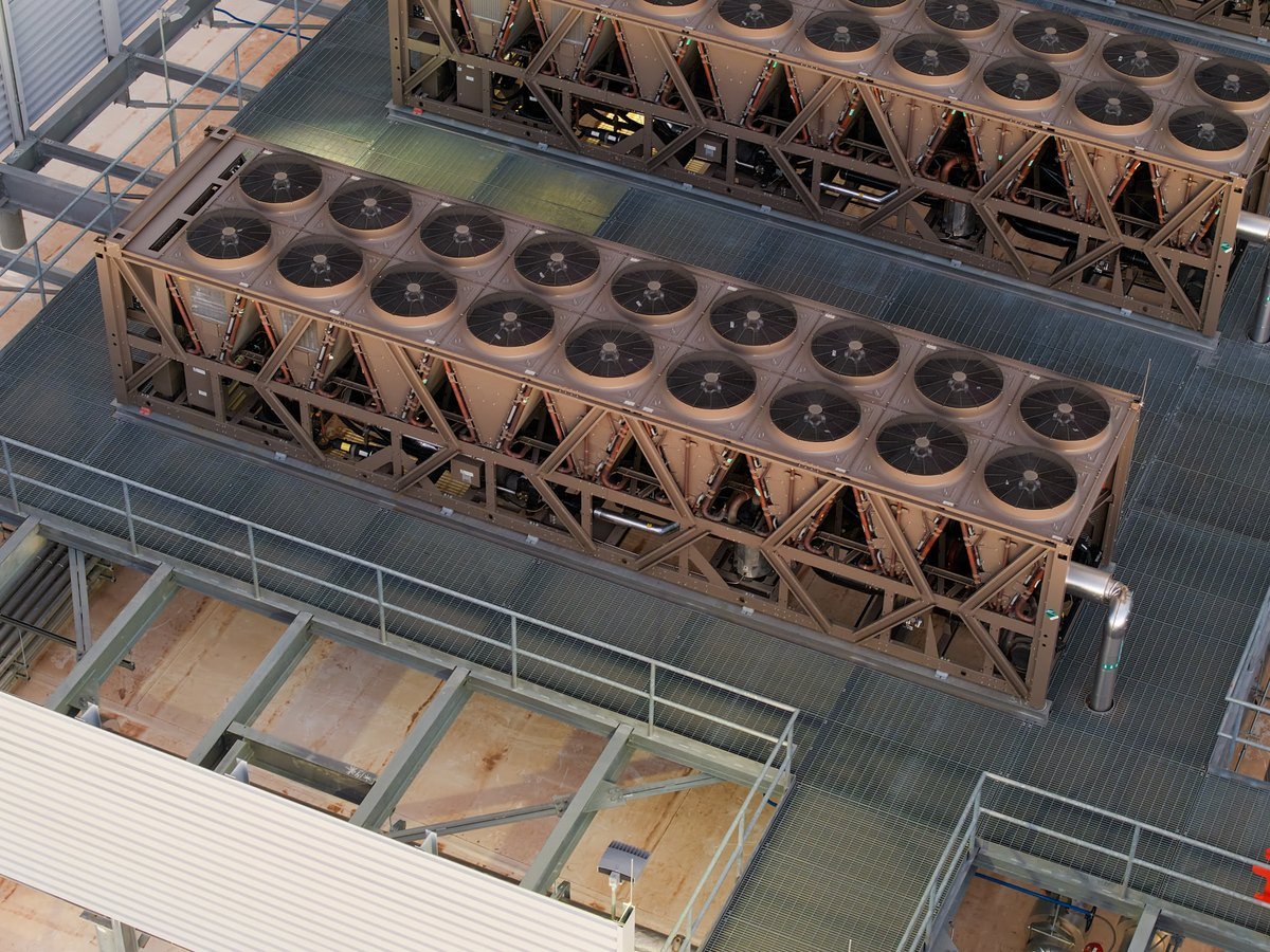 Rows of large industrial air-cooled chillers on a data centre roof deck, seen from above.