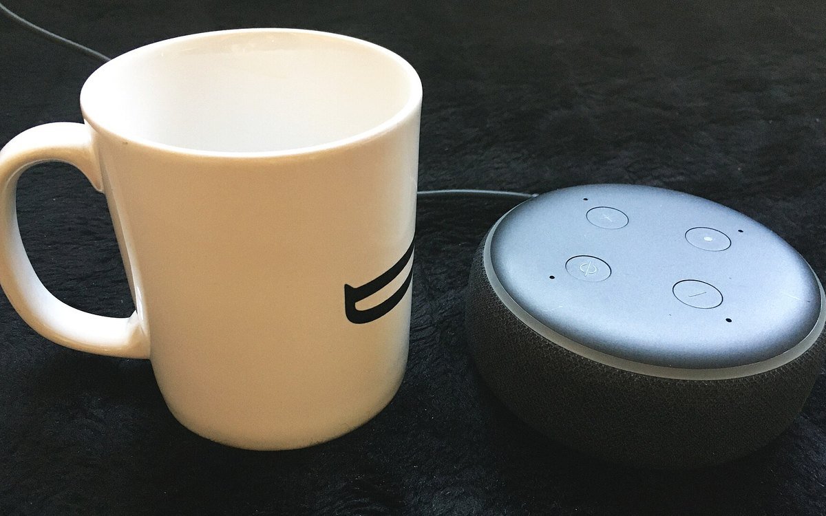 An Amazon Echo Dot next to a coffee mug of similar height on a dark table