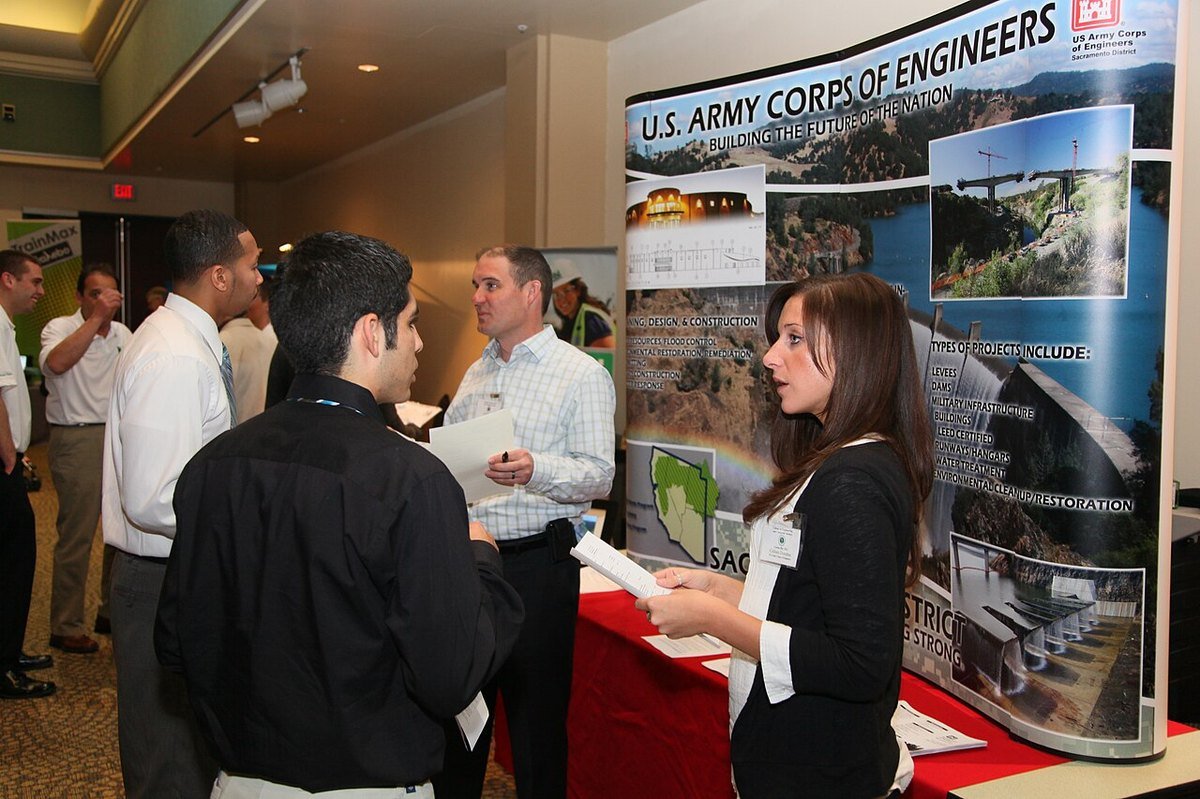 Students in business clothes talking with engineers in front of a U.S. Army Corps of Engineers display