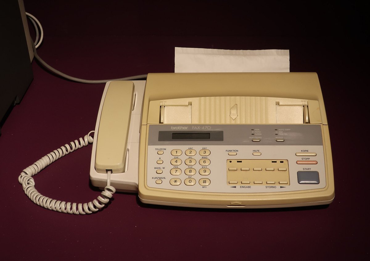 A beige 1990s-era Brother FAX-470 fax machine with a sheet of paper feeding out of the top.