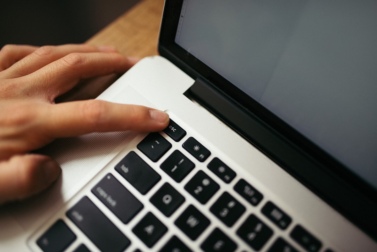 Close-up of a finger pressing a key on a silver laptop keyboard.