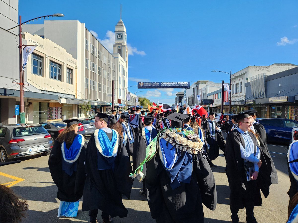 University graduates in academic gowns and hoods walking in a graduation procession down a city street