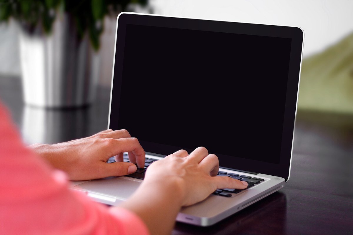 Two hands typing on a silver laptop keyboard at a dark wooden desk.