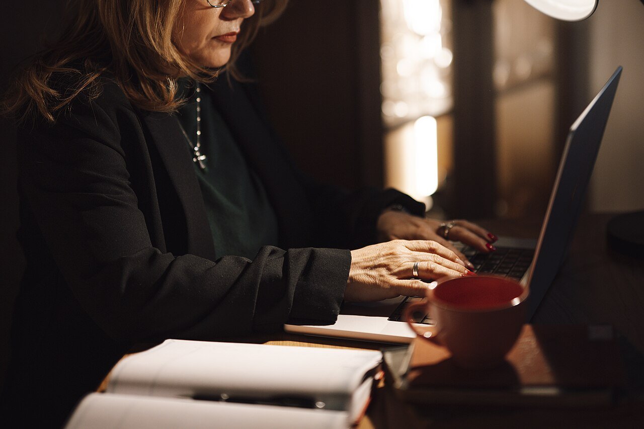 A woman working on a laptop at a desk in a dimly lit home office