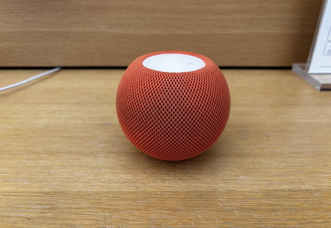 An orange HomePod mini on a wooden shelf