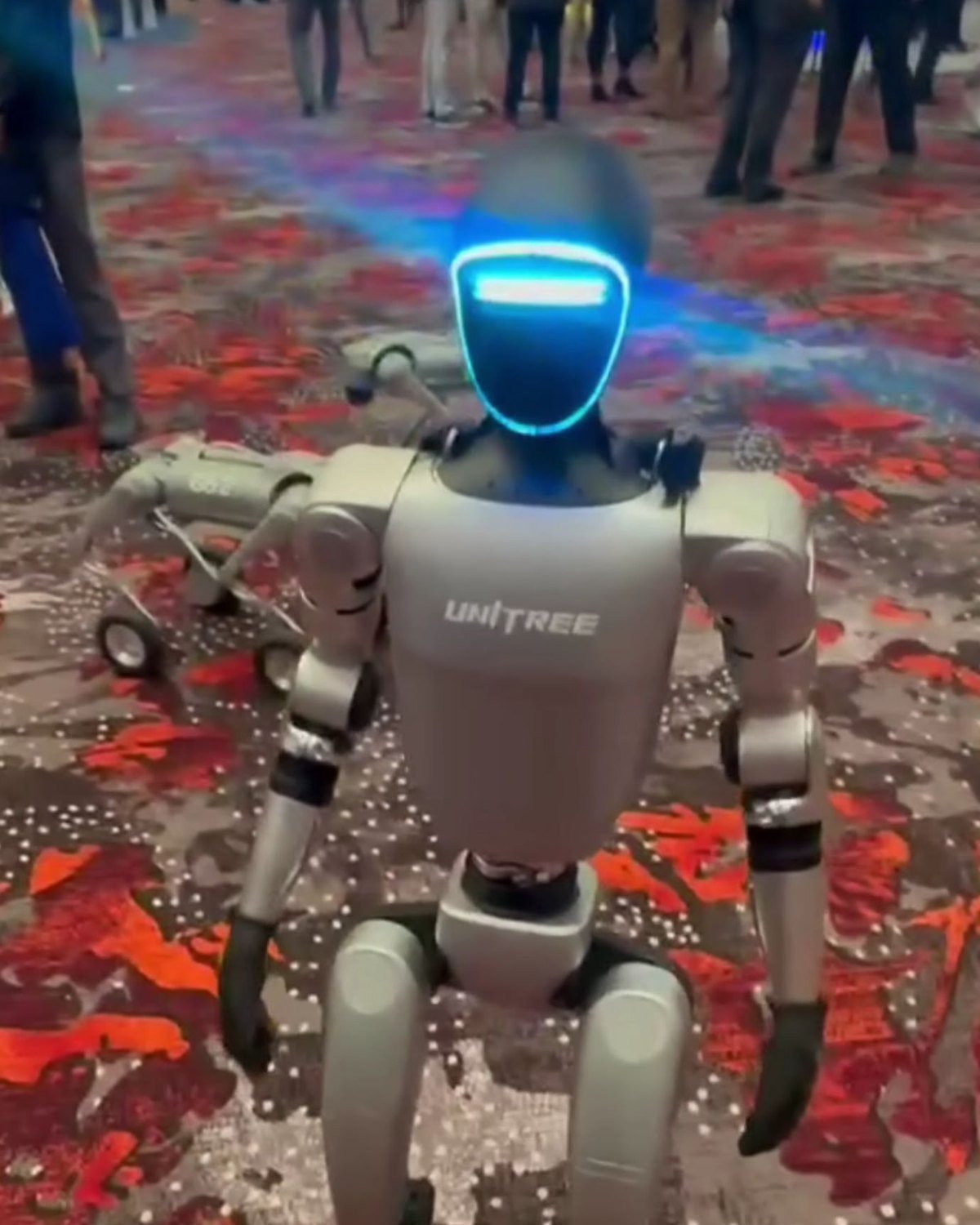 A Unitree G1 humanoid robot standing on a patterned carpet at a trade show
