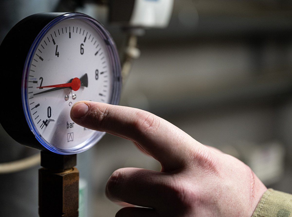 A technician's finger pointing at a pressure gauge on mechanical plant equipment
