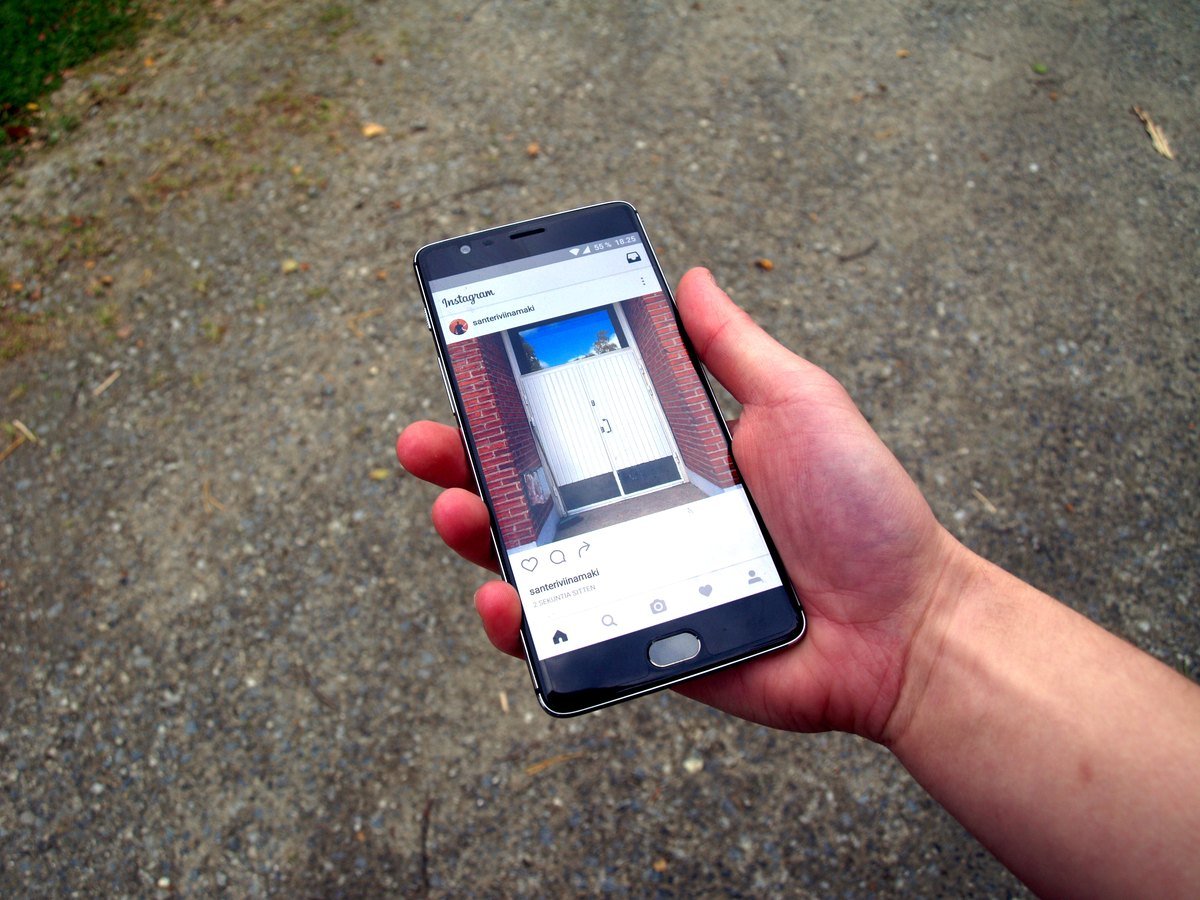 A hand holding a phone showing an Instagram photo feed.