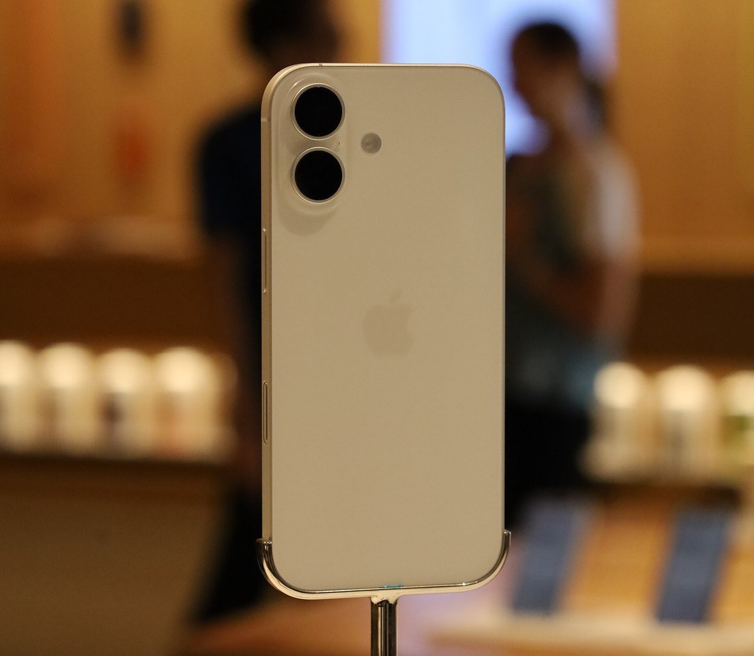 An iPhone on a security stand in an Apple Store, shoppers blurred in the background