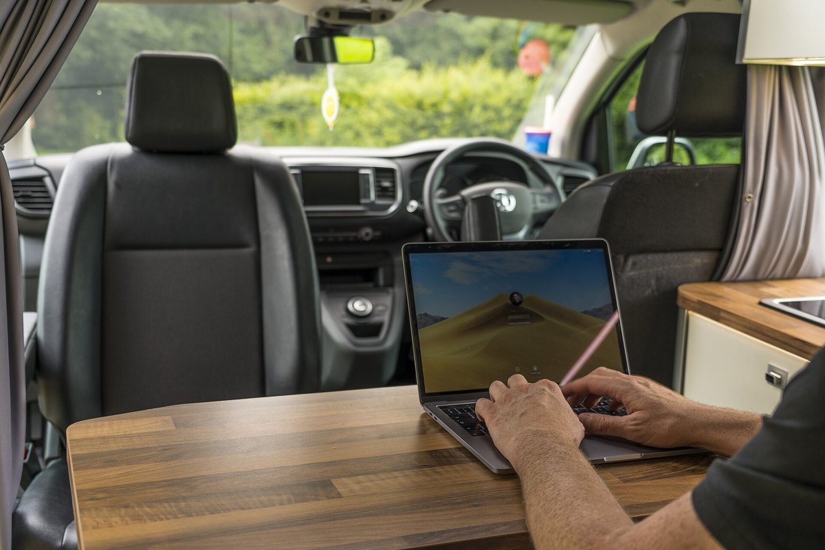 Man typing on a laptop at a table inside a camper van