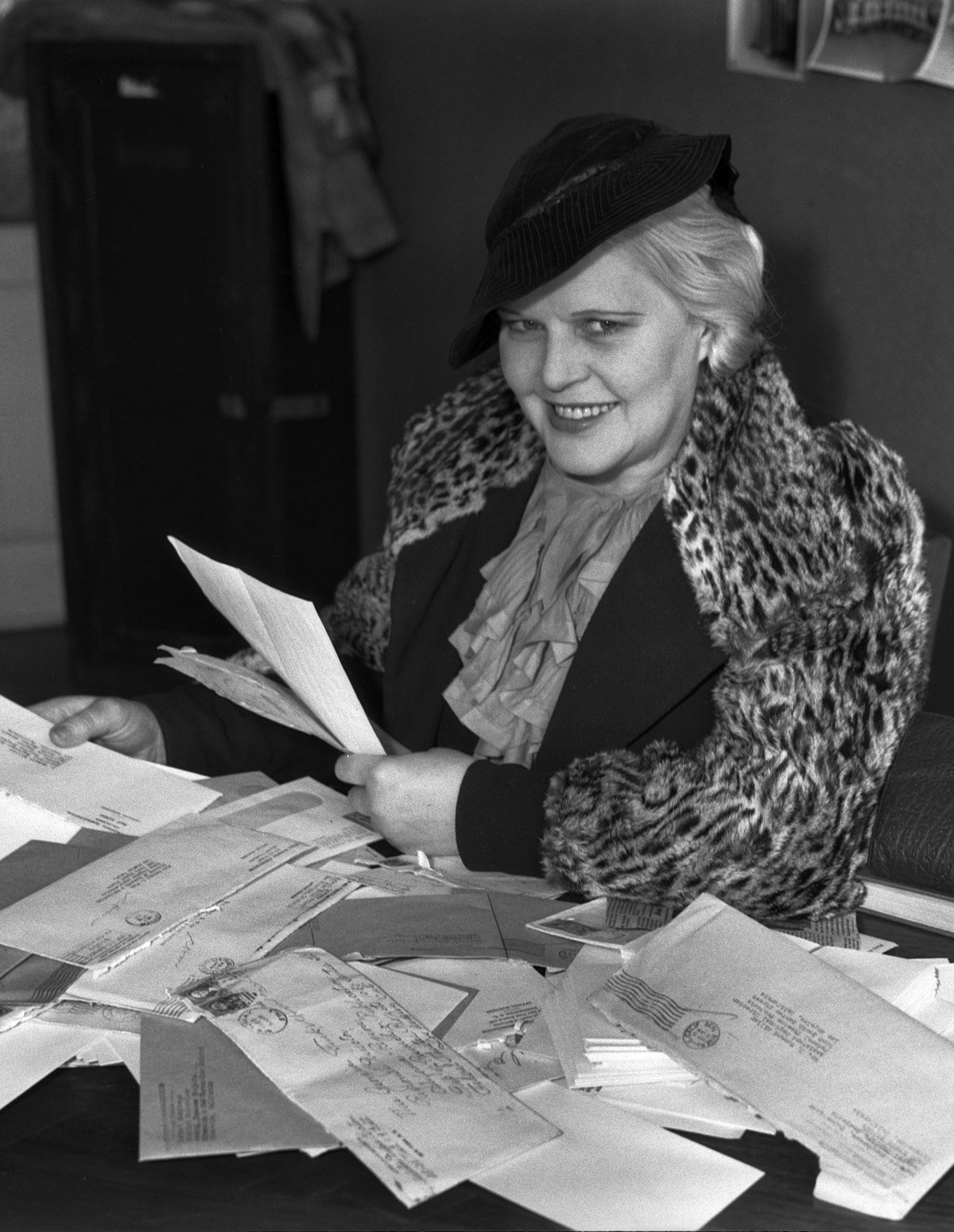 A woman in 1936 reading through a large pile of letters at a desk.