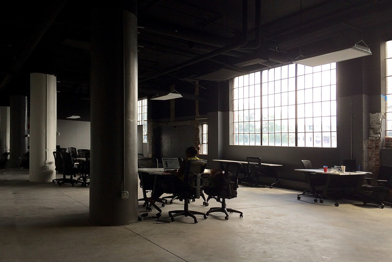 A nearly empty open-plan office with a single worker at a laptop