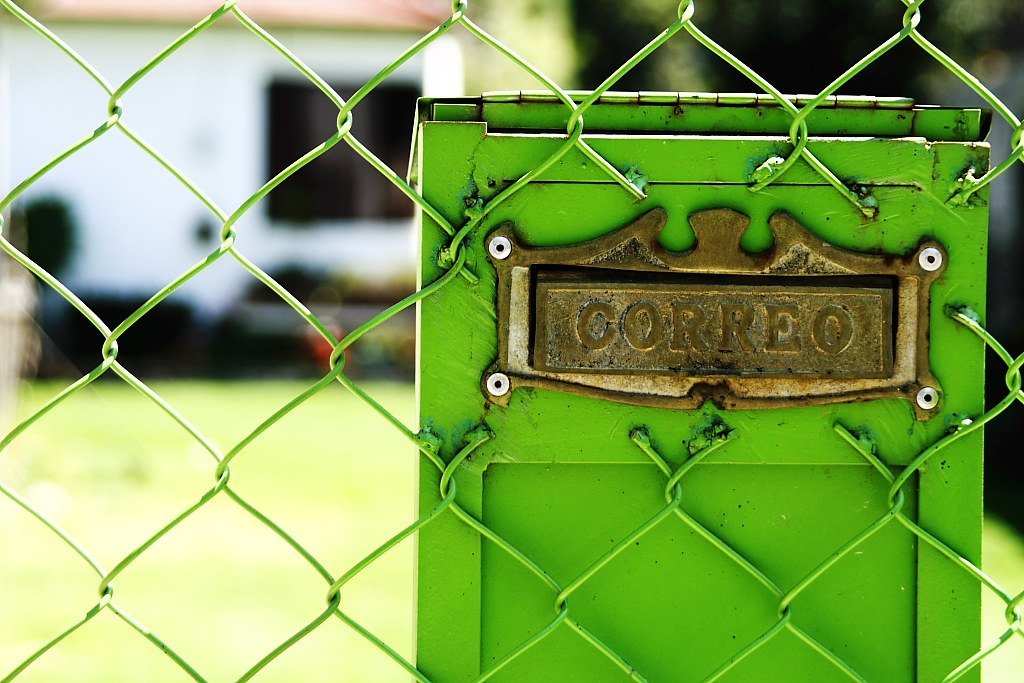 A green metal mailbox marked CORREO behind a chain-link fence