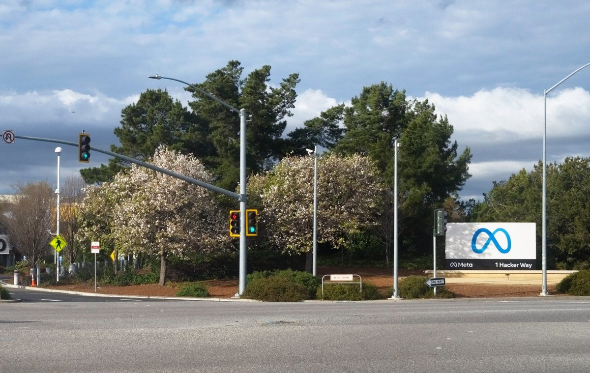 The Meta sign at 1 Hacker Way, Menlo Park, California, beside a road and trees.