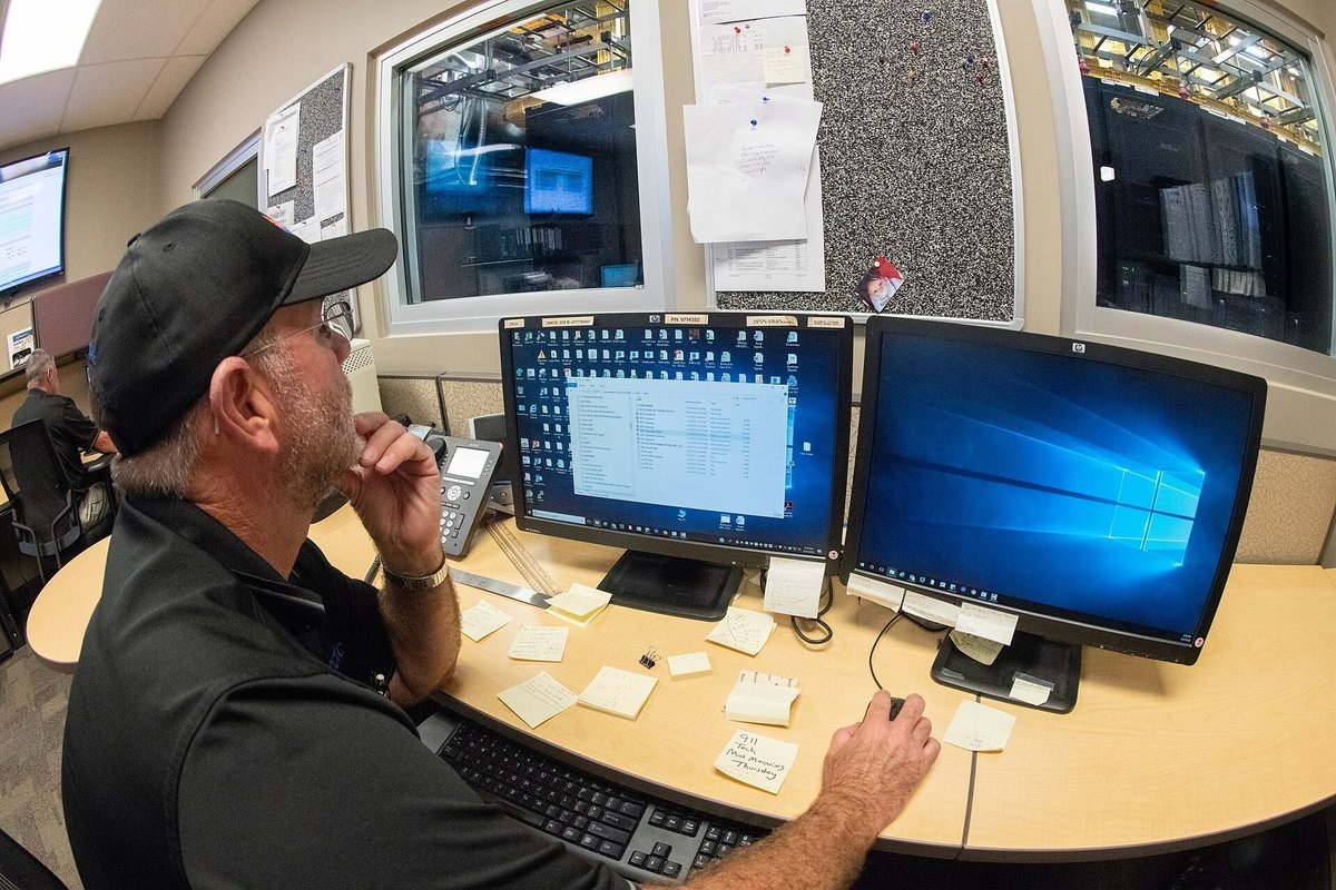 A technician at a network operations centre desk with several monitors, reading a notification.