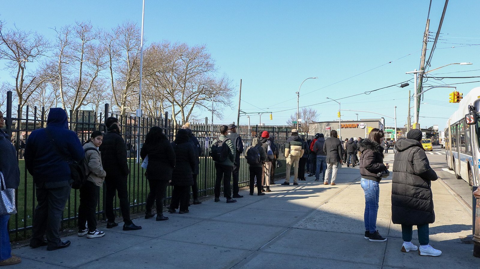 Job applicants lined up along an iron fence outside a New York City transit job fair on a clear winter day